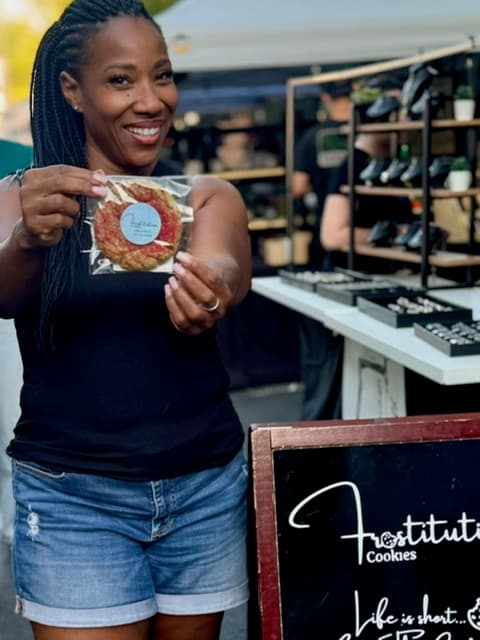 Dana Byrd, Head Frostitute of Frostitution Cookies, smiling at a market holding a packaged cookie